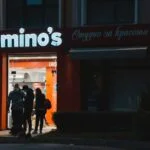 a group of people standing outside of a domino's store
