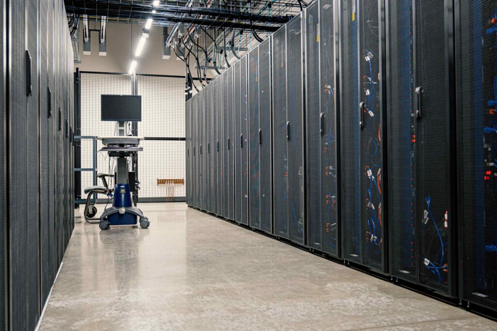 A long corridor in a modern data centre lined with steel server racks, networking equipment and cables